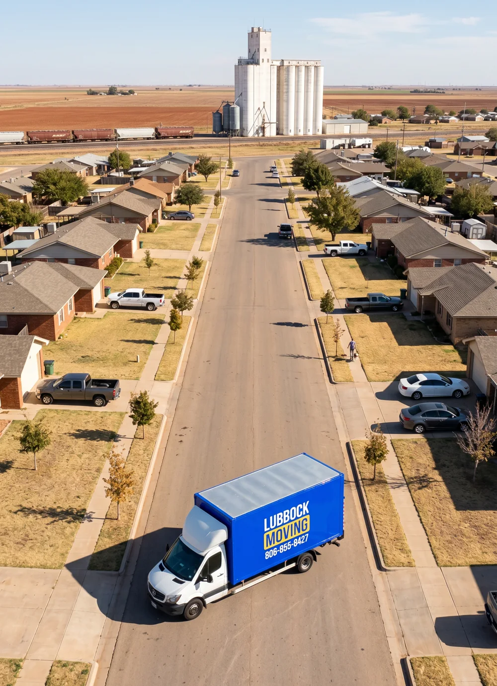 Lubbock Moving Company blue moving truck on a residential street in Shallowater, Texas with grain elevators and the railroad in the distance